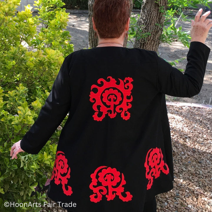 Back view on model of black swing jacket on model, showing one large red embroidered pattern in center back and three large complimentary patterns along the bottom