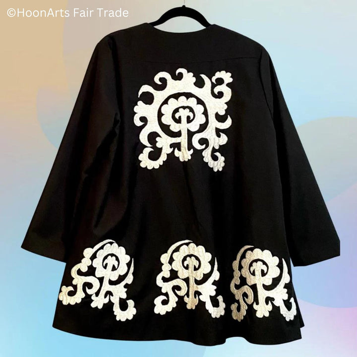 Back view of black swing jacket, with large white hand embroidery pattern in center back and three smaller hand embroidery ornaments long the bottom